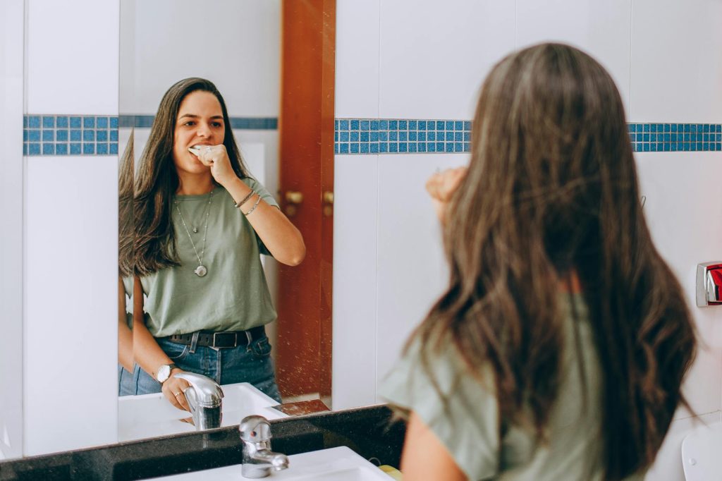 Uma jovem escova os dentes, olhando-se no espelho do banheiro. Conceito de autocuidado e higiene.
